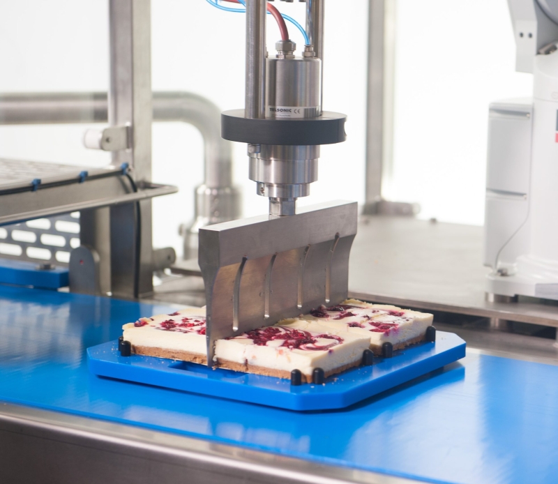 Ultrasonic Cutting Blade Cutting into Square Cheesecake on Blue Cutting board
